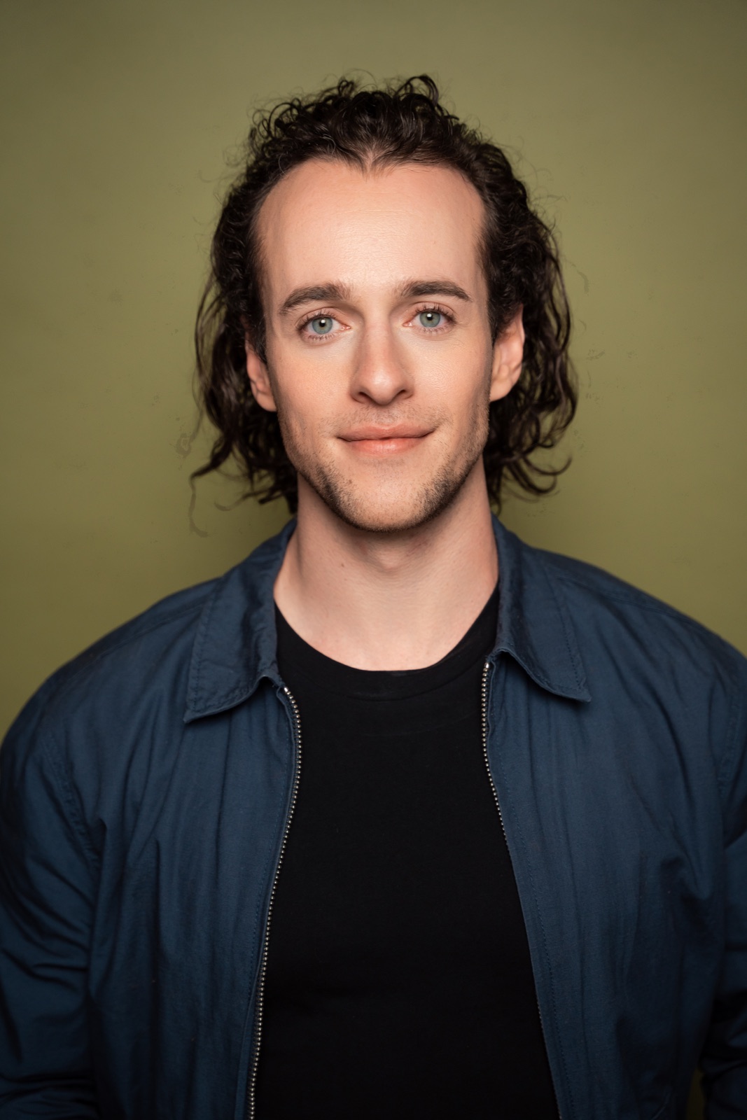 Abe Watson in a blue jacket against an olive-green background.