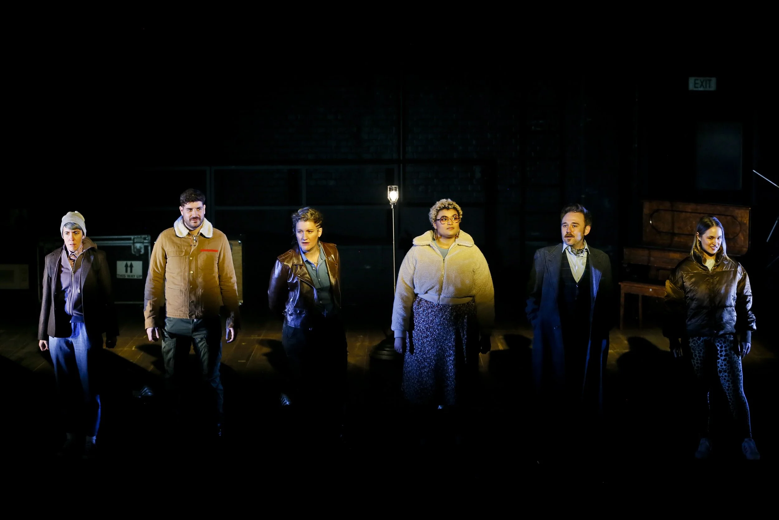 Six performers stand in a line across the dimly lit Cyrano stage.