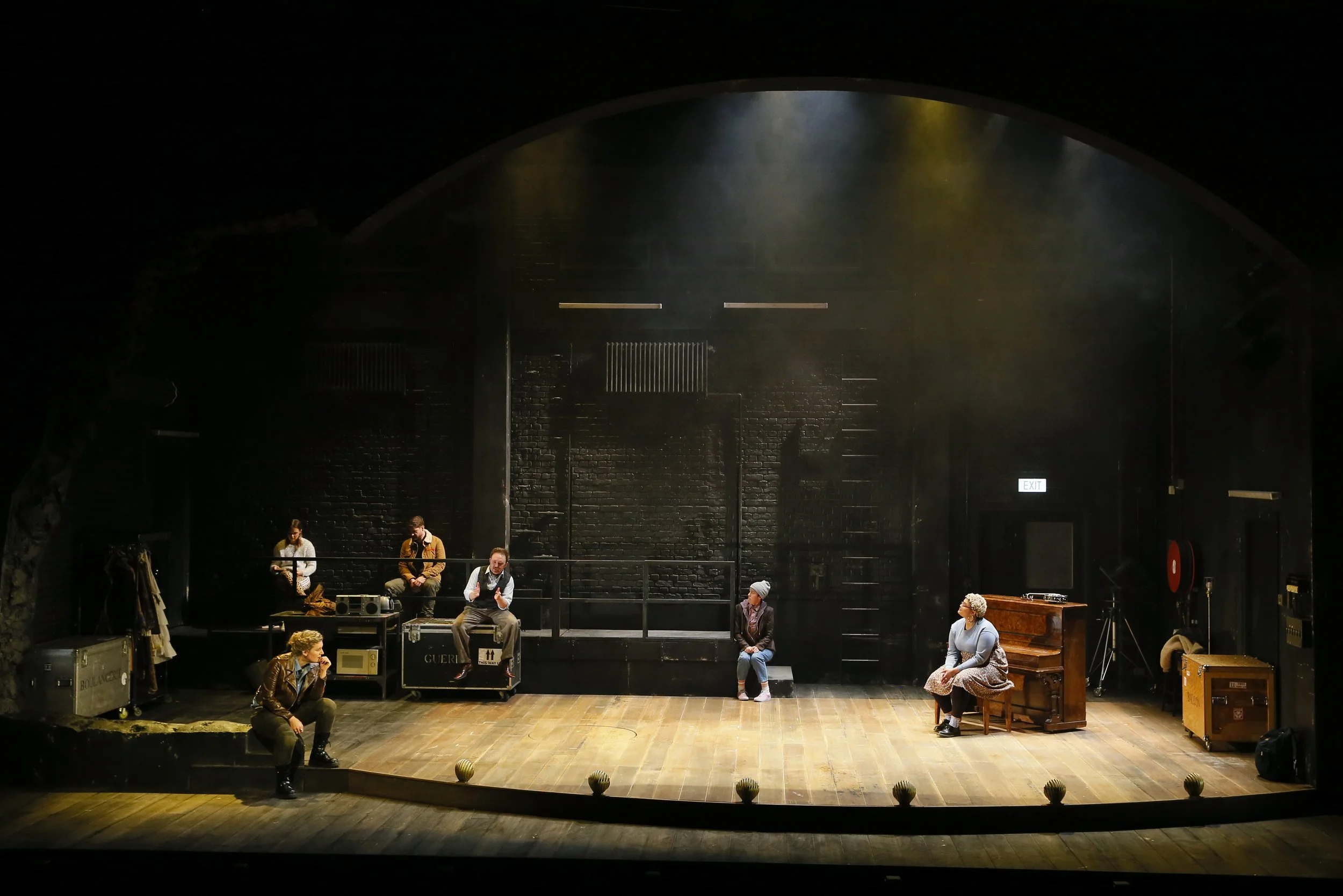 Wide view of the Cyrano stage, with performers, a piano and backstage scenery.