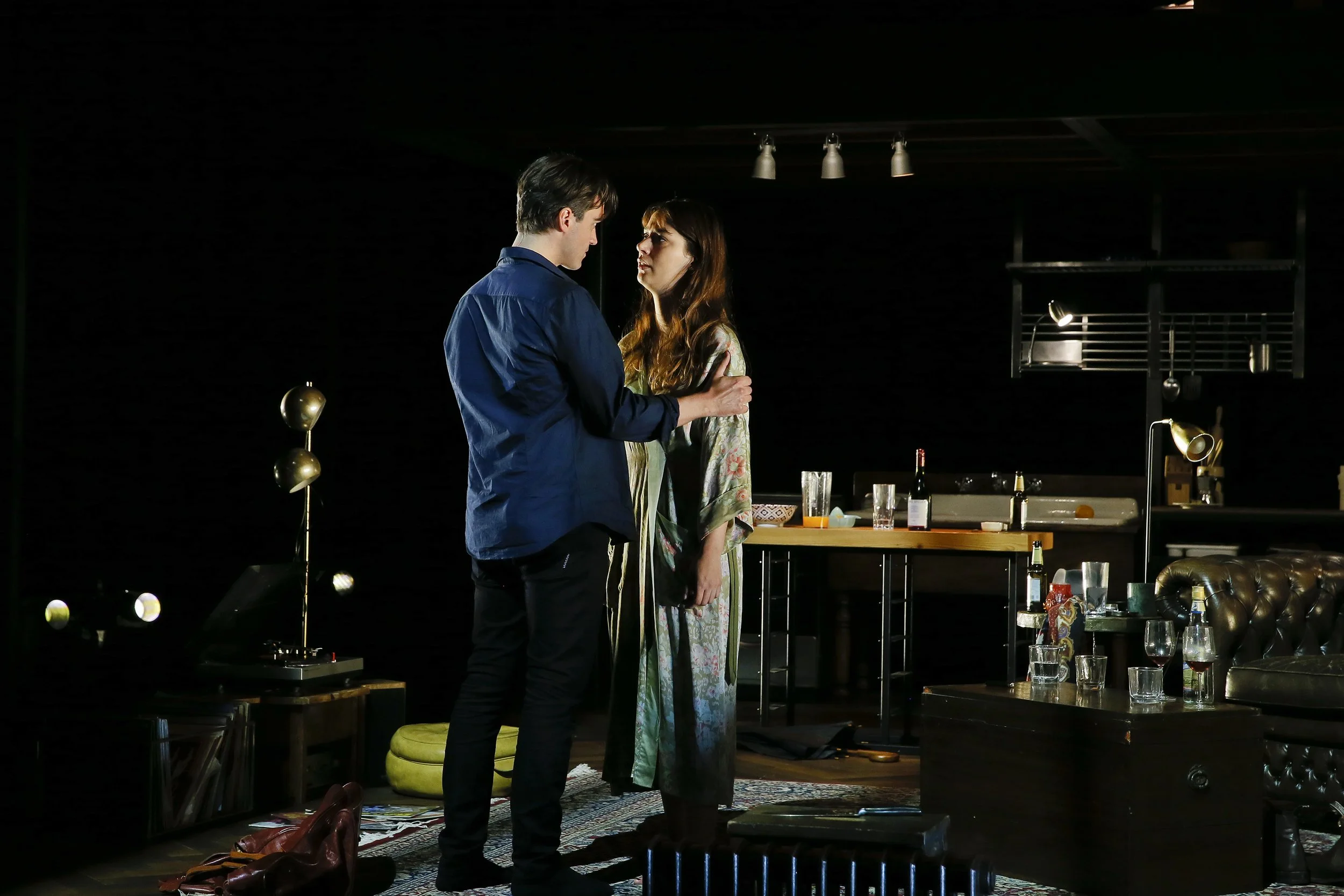 Two Berlin performers face each other beside the dining table.