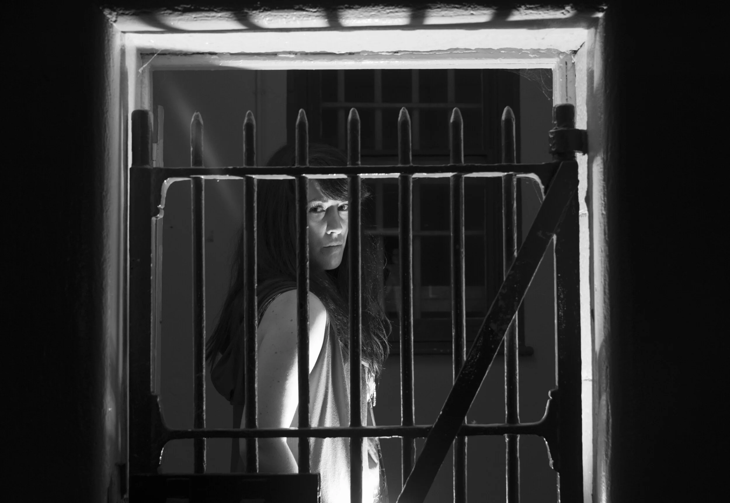 Black-and-white Assassins portrait of a performer behind a barred doorway.