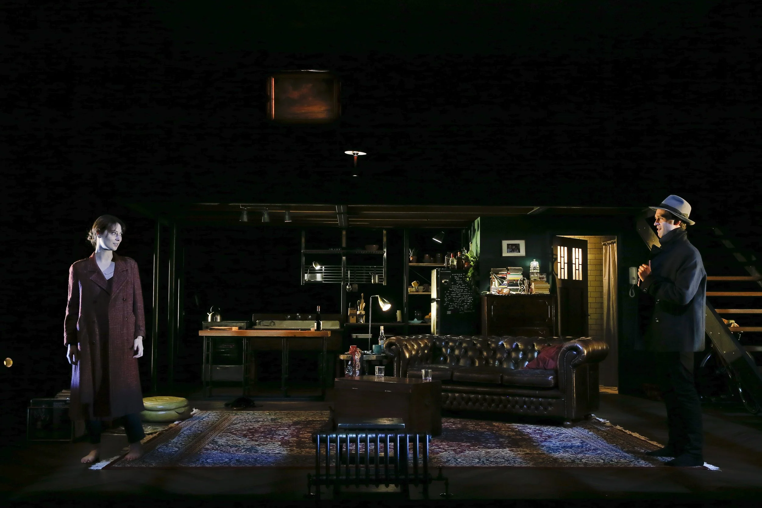 Two Berlin performers stand apart across the darkened apartment set.