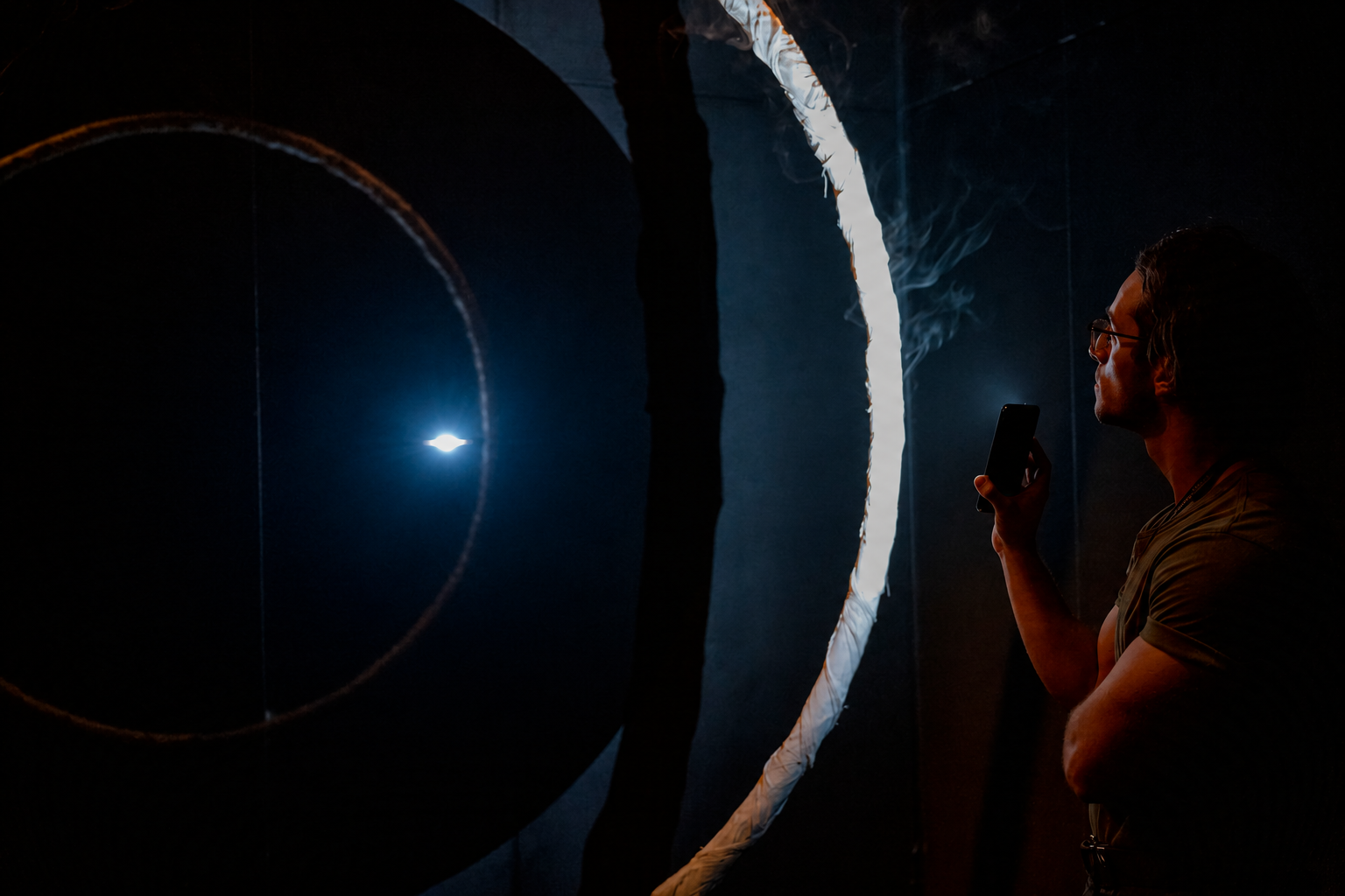 Abe Watson holding a phone torch beside the smoking ring in the Australian ECR exhibition at PQ2023.