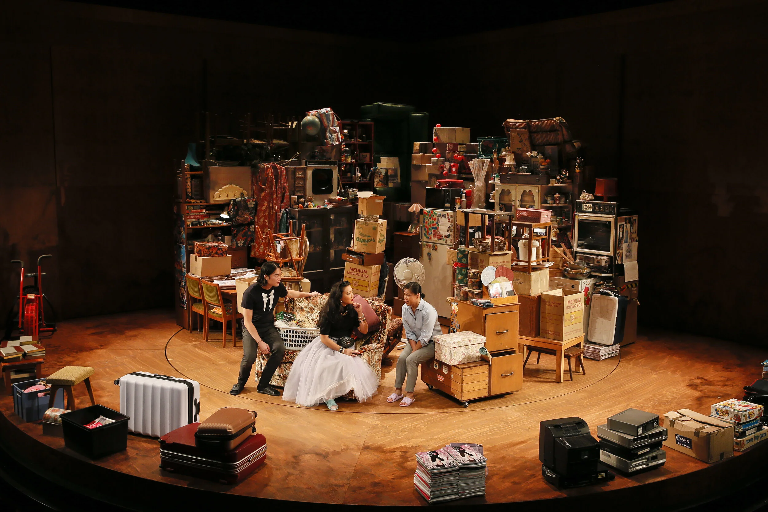 Wide view of Torch the Place, with performers surrounded by stacked boxes, shelves and household possessions.